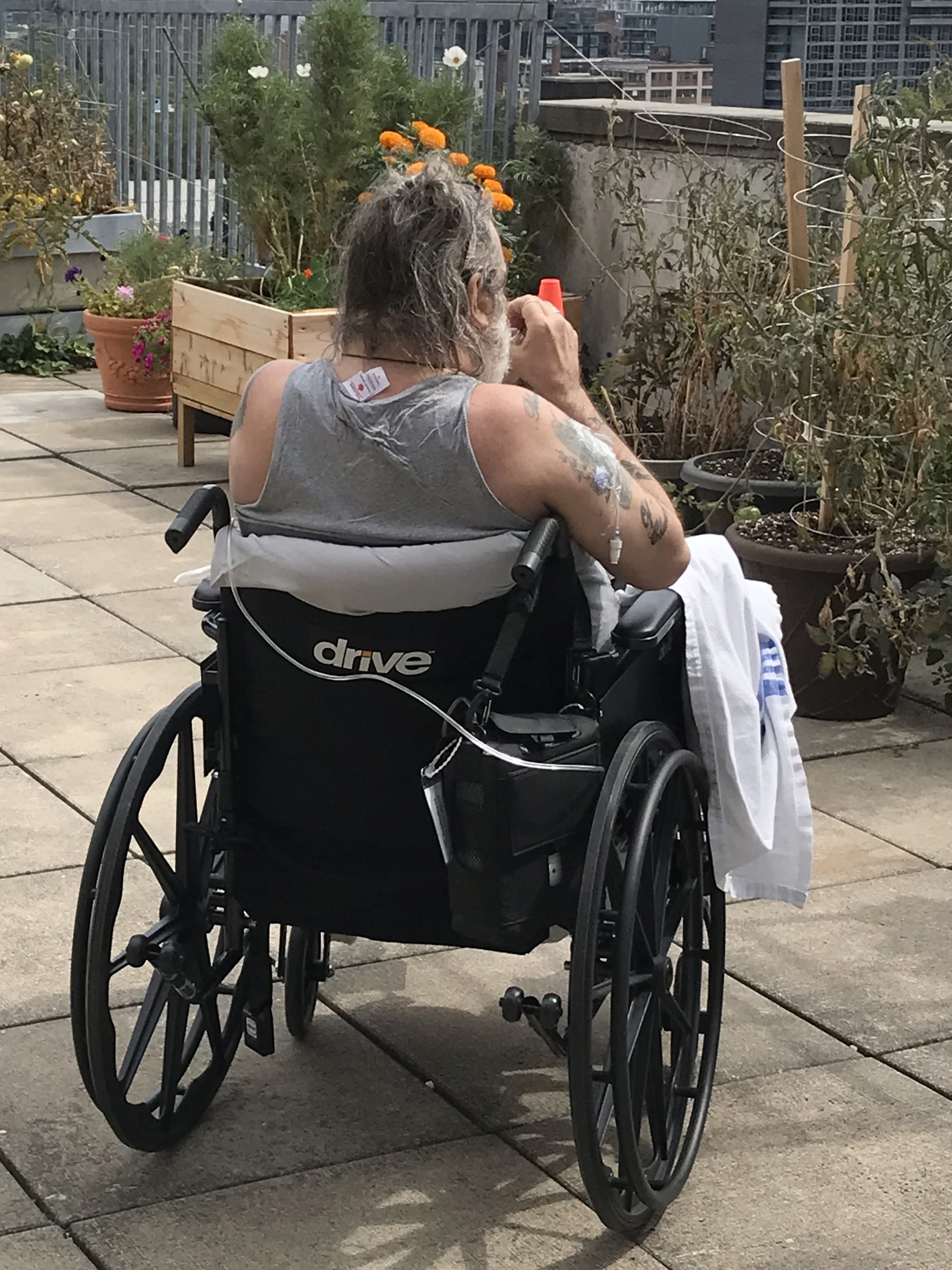 A patient in a wheelchair faces away from the camera and looks off the roofline to the city views.